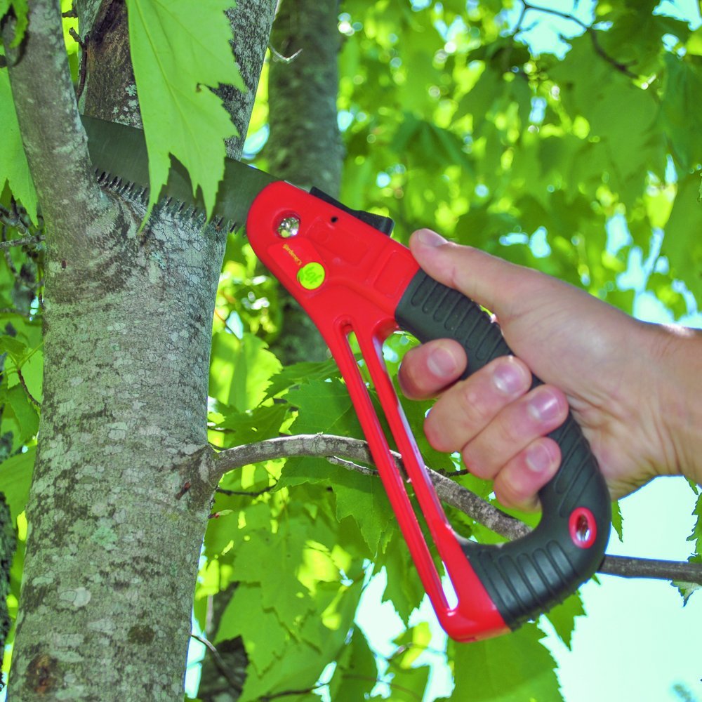 A hand holding a red pruning saw and cutting a tree branch