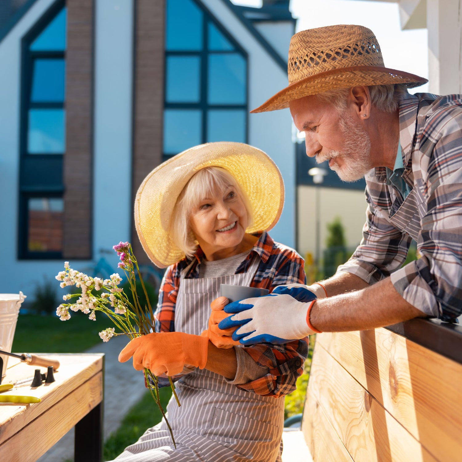 Elderly smiling couple sat on a garden bench in the sunlight arranging flowers