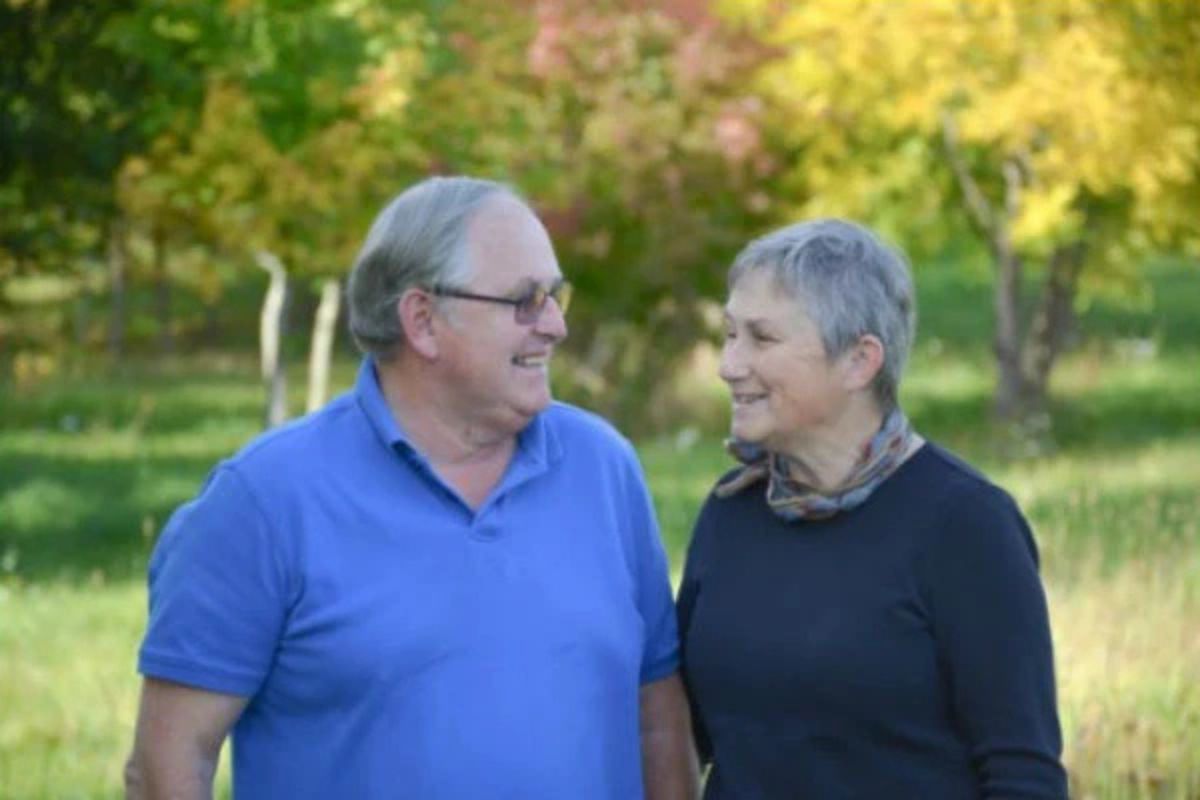 Paul and Nancy Grimm, the founders of TGF. The couple are wearing blue tops and smiling at each other against a backdrop of a green woodland