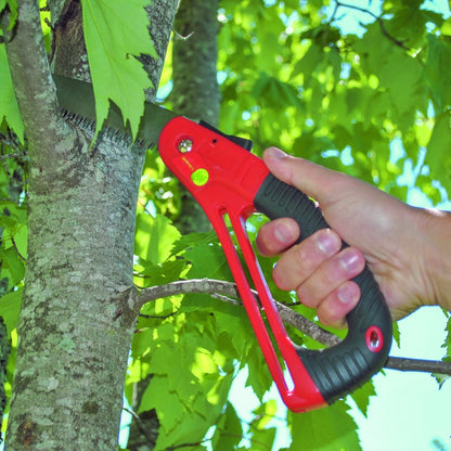 A hand holding a red pruning saw and cutting a tree branch