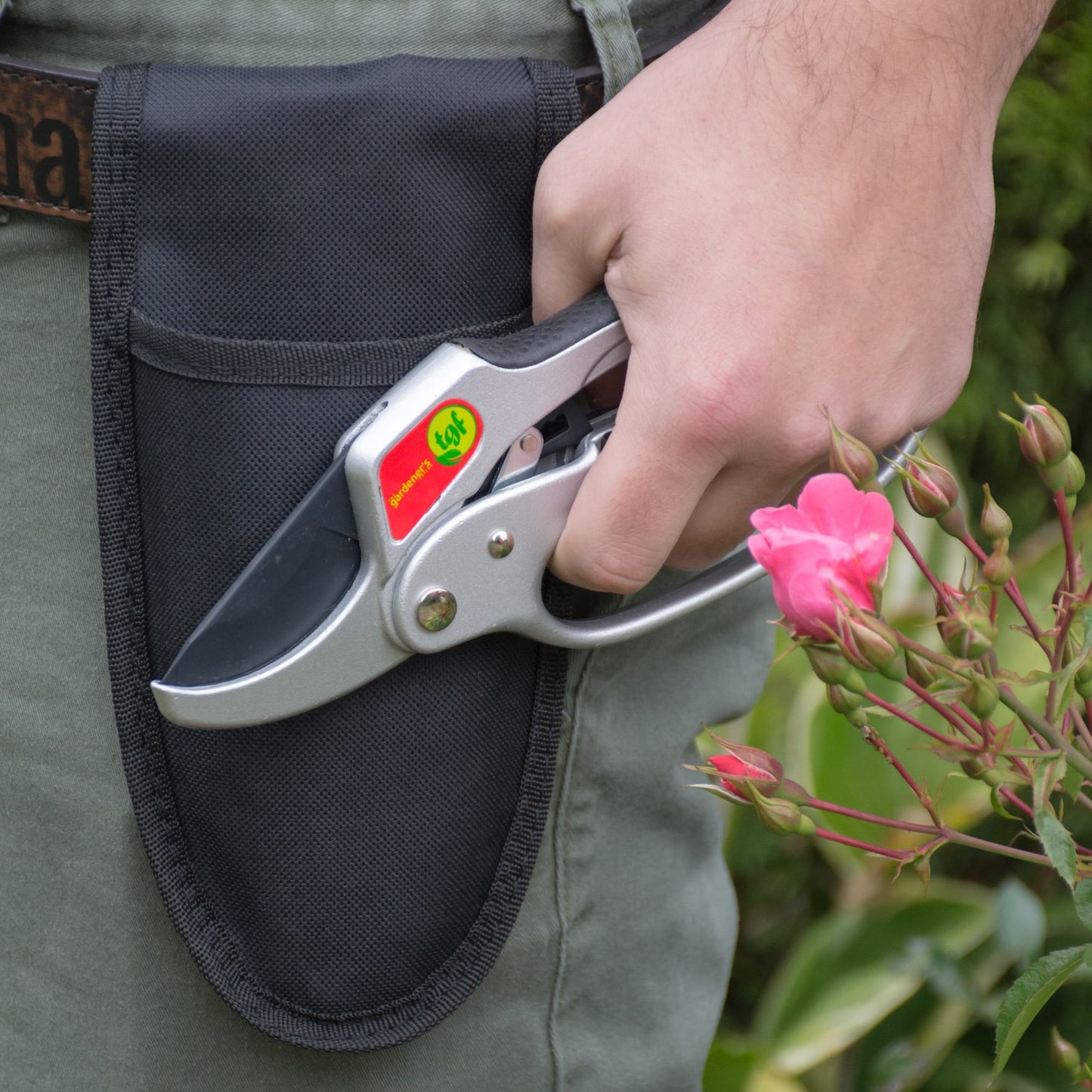 Mans hand holding ratchet pruners by his side in front of a holster attached to his belt